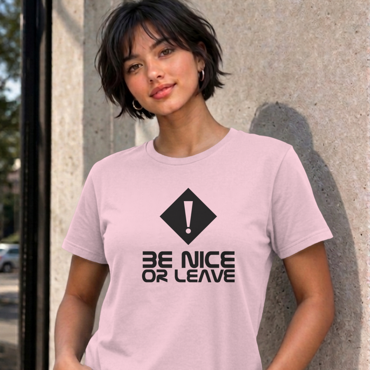 Woman wearing the light pink Be Nice or Leave graphic tee